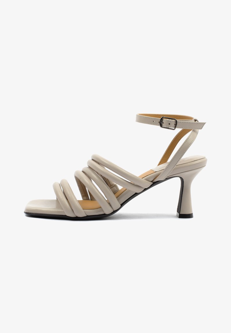 Sandalo con tacco beige a punta quadrata, con più cinturini curvi e una sottile cinghia alla caviglia con fibbia. Finitura in pelle texturizzata.
