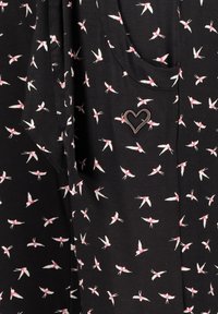 Svart tyg med ett upprepat mönster av små vita fåglar med rosa detaljer. Inkluderar en metallisk hjärtformad prydnad.