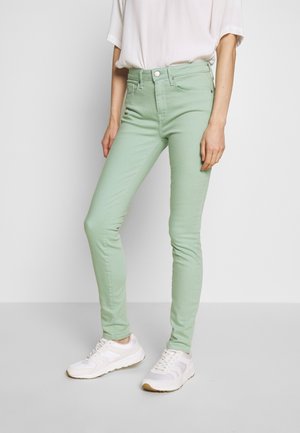 Pantalones ajustados verde menta hechos de una mezcla de algodón, con una cintura alta, cinco bolsillos y un cierre de botón y cremallera. Combinados con zapatillas blancas.