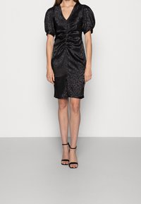 Black dress with leopard pattern, V-neck, puff sleeves, and ruching detail. Knee-length with a slight slit. Paired with black ankle strap sandals.