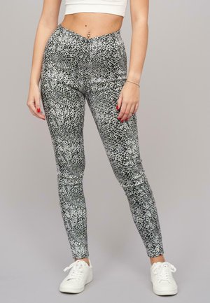 Leggings taille haute en imprimé serpent noir et blanc. Tissu extensible et texturé avec une finition lisse, associés à des baskets blanches.