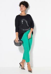 Haut noir avec un design de cœur en sequins, manches 3/4 ; associé à un pantalon slim vert avec un motif subtil ; accessoirisé avec un sac noir et des escarpins argentés.