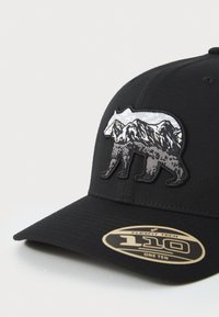 Casquette noire en tissu avec un design en broderie d'un ours argenté et d'une montagne à l'avant. Comprend un autocollant de logo circulaire sur la visière.
