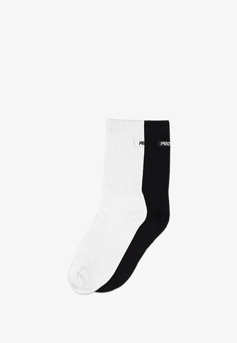 Skarpety z mieszanki bawełny w kolorze białym i czarnym, o prążkowanej fakturze, długości do połowy łydki, z nazwą marki "PROS" na czarnej skarpecie.