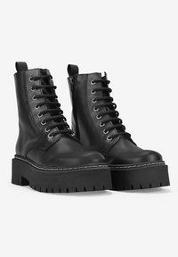 Botas de cuero negras hasta el tobillo con una suela de plataforma gruesa, parte delantera con cordones y cremallera lateral. Presenta costuras prominentes y una suela texturizada.