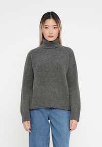 Pulover gri cu gât înalt dintr-un tricot moale, cu o croială lejeră și manșete nervurate, asortat cu blugi albaștri cu talie înaltă.