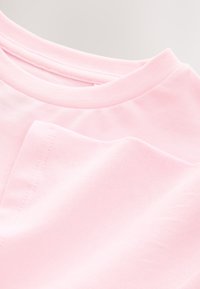 Tricou roz deschis din bumbac, cu decolteu rotund și mâneci scurte, având un finisaj neted și detalii vizibile de cusătură pe tiv.