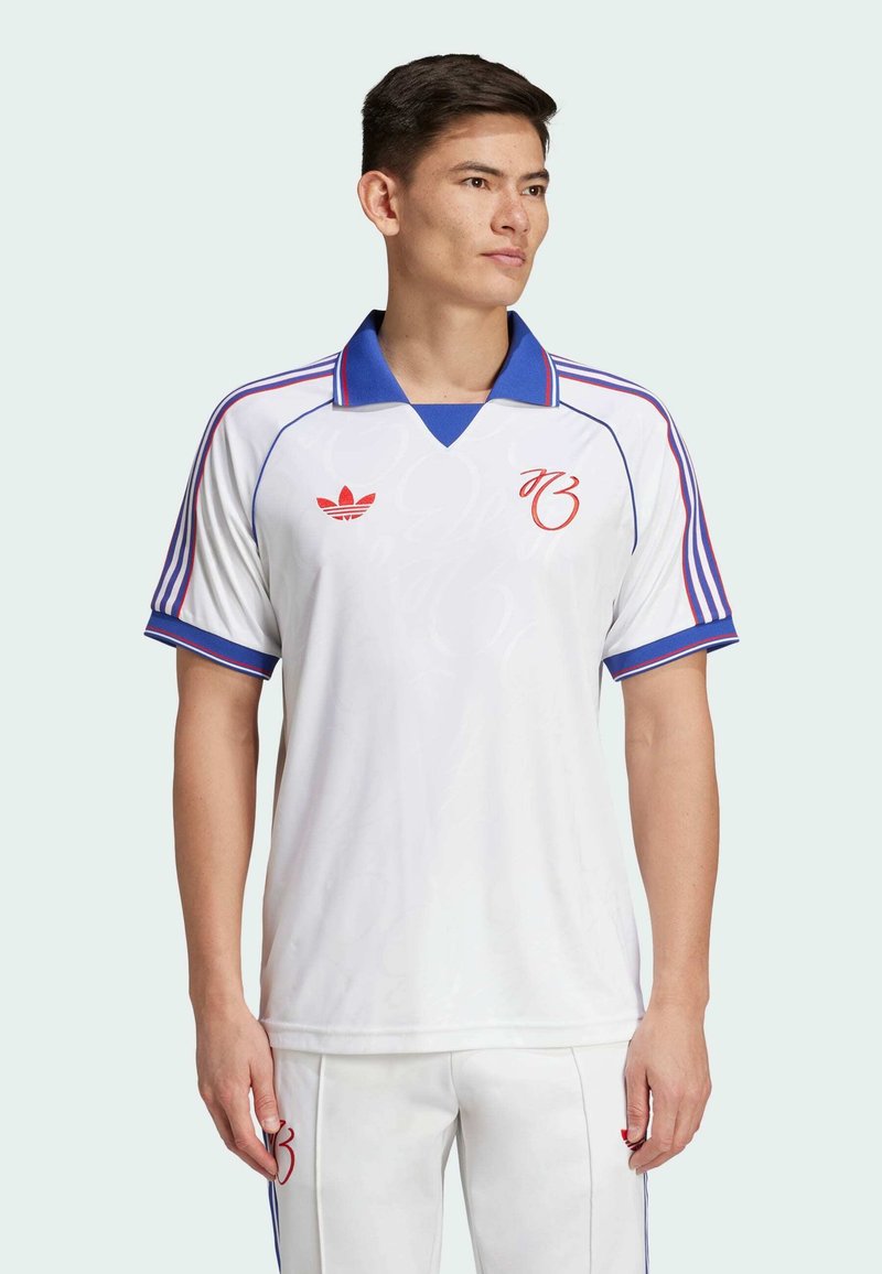 Biela športová košeľa s modrým golierom a červenými akcentami. Ikonické tri pruhy na rukávoch a jemný vzor na látke. Zobrazené logo Adidas.