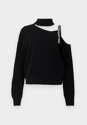 Black sweater with a high neck, one shoulder exposed, and a prominent strap reading "Karl Lagerfeld." Textured knit with ribbed cuffs.