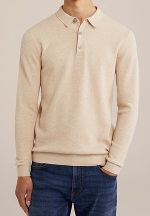 Beige polotrui met lange mouwen en een gestructureerd breipatroon, drie knopen en geribbelde manchetten. Draagt dit over donkerblauwe spijkerbroek.