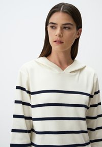Hoodie in Creme mit marineblauen horizontalen Streifen, mit einer weichen Textur und einem bequemen Schnitt. Mit gerippten langen Ärmeln.