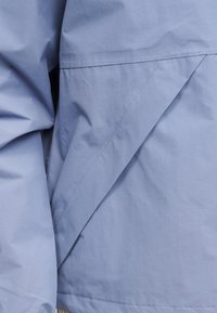 Ανοιχτό μπλε ύφασμα με ορατή ραφή και διπλωμένη λεπτομέρεια, πιθανότατα μέρος του μανικιού και του σώματος ενός ρούχου.