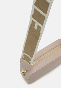 Světle růžová kožená taška se zlatým zipem. Popruh má béžový textilní design se světle zelenými akcenty a geometrickými vzory.