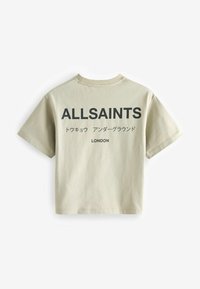 Bézs rövid ujjú póló fekete nyomott „ALLSAINTS”, japán szöveg és „LONDON” felirattal a hátoldalán.