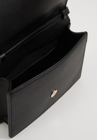 Černá kožená kabelka otevřená, aby ukázala vnitřní přihrádky a zlaté magnetické zapínání na předním klopě.