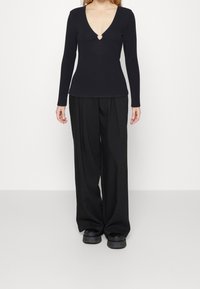 Musta pitkähihaine paita syvällä V-puolella, jossa on hopeinen sydämenmuotoinen leikattu osa. Yhdistetty leveälahkeisiin mustiin housuihin ja tukeviin mustiin kenkiin.