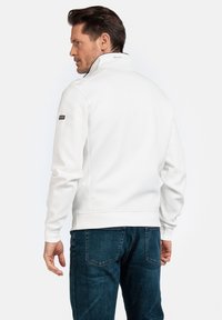 Witte sweatshirt met hoge kraag, ribgebreide manchetten en zoom. Bevat een klein logo op de linker mouw en heeft een gladde textuur. Gecombineerd met blauwe spijkerbroek.