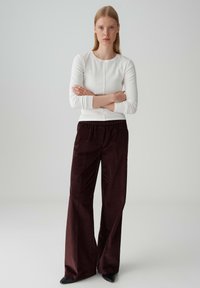 Maglietta bianca a maniche lunghe con scollo rotondo e tessuto testurizzato, abbinata a pantaloni in corda larghi di un intenso bordeaux. Design fluido e morbido.