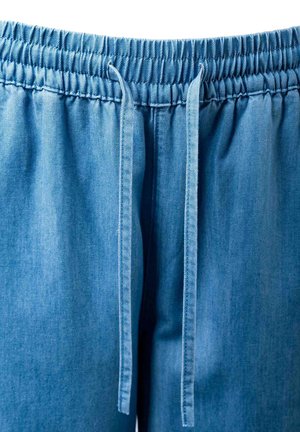 Pantalones de mezclilla azul claro con cinturilla elástica y cordones largos que cuelgan en el centro frontal.