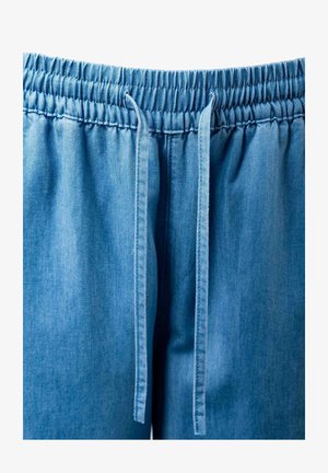 Šviesiai mėlynos džinsinės kelnės su elastine juosmens juosta ir ilgomis raištelėmis, kabančiomis priekyje centre.