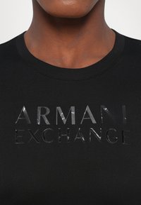 Black cotton t-shirt with a crew neck featuring a glossy "ARMANI EXCHANGE" logo in textured, reflective material.