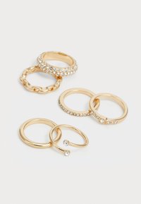 Conjunto de anéis de ouro com vários designs: uma banda larga com strass, um elos de corrente, e vários estilos lisos e com miçangas.