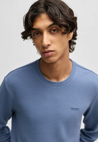 Blauwe lange mouwen shirt met een gestructureerd patroon, voorzien van een ronde hals en een subtiele geborduurde logo op de borst. Zachte stof.