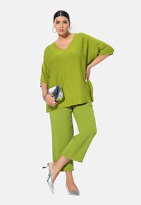 Limoengroene oversized V-hals top gecombineerd met bijpassende cropped broek, aangevuld met zilveren slingback hakken en een metalen clutch.
