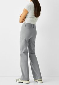 Graue, weite Hose aus glattem, strukturiertem Stoff mit hoher Taille und Gürtelschlaufen. Kombiniert mit hellen Sneakers.