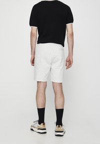 Chemise noire à manches courtes avec des accents blancs, associée à un short gris clair. Les chaussures présentent un schéma de couleurs beige, noir et gris. Fond uni.