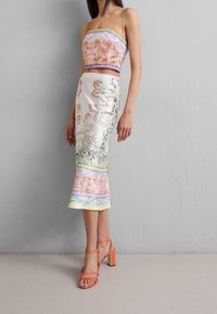 Ensemble deux pièces comprenant un haut court à motif floral et une jupe longue à ourlet évasé. Couleurs : rose, vert et blanc. Sandales à talons blocs orange.