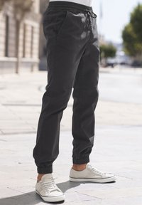 Zwarte joggingbroek met een elastische tailleband, koord, zijzakken en gerimpelde manchetten, gecombineerd met witte sneakers.