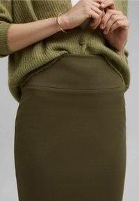 Olijfgroene midi pencil skirt gemaakt van rekbaar materiaal, met een hoge tailleband en een gladde textuur, gecombineerd met een losgebreide groene cardigan.