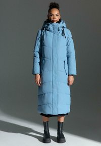 Padded long coat in light blue, featuring a high neck hood, zip closure, side pockets, and black accents, with a quilted design.