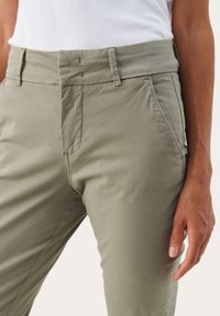 Pantalons kaki en tissu léger et lisse ; dotés d'un zip, de poches avant et d'une coupe ajustée. Fini texturé avec des détails de couture subtils.