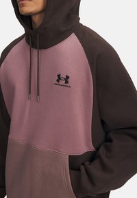 Sweat à capuche en marron et mauve, présentant un design à blocs de couleur contrastants, des cordons de serrage et un logo Under Armour sur la poitrine.