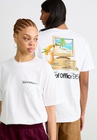 Weißes Baumwoll-T-Shirt mit einem Grafikdesign auf dem Rücken: Ein Vintage-Computer mit einer tropischen Szenerie und einem Papagei. Kleines Textlogo auf der Vorderseite.