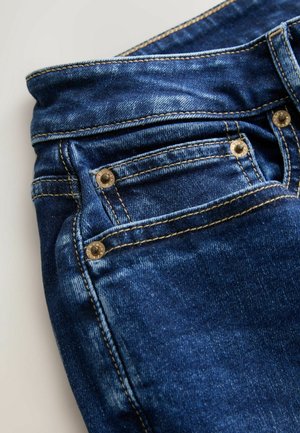 Nærbillede af blå denimjeans med forlomme, nitter, syninger og linning på en hvid baggrund.