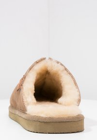 Brown suede slipper featuring a wide opening, soft cream fur lining, and a flat, textured beige sole. No visible hardware or patterns.