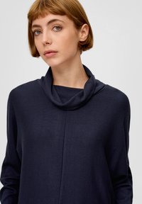 Donkerblauw coltrui gemaakt van gestructureerde stof, met een relaxte pasvorm en lange mouwen, en een eenvoudige naaddetail aan de voorkant.