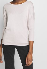 Light pink, ribbed knit sweater with three-quarter sleeves and a rounded neckline. Soft texture and relaxed fit design.