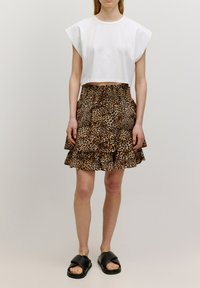 Weißes, kurz geschnittenes T-Shirt mit kurzen Ärmeln, kombiniert mit einem braunen Leopardenmuster-Rüschenshirt und schwarzen Slides mit breiten Riemen.