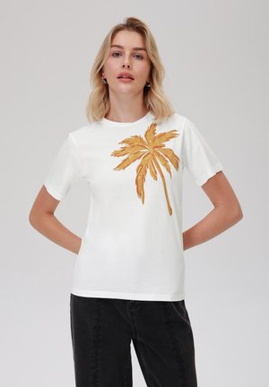 Weißes Baumwoll-T-Shirt mit einem großen goldenen Palmenbaum-Design auf der Vorderseite. Kurze Ärmel und ein lässiger Schnitt, kombiniert mit dunklen Jeans.