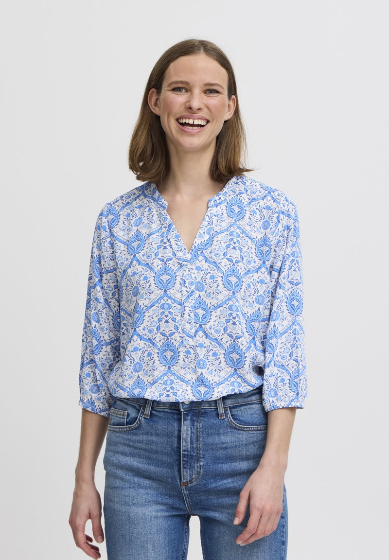 Blusa blu con motivo floreale, scollo a V e maniche a tre quarti, realizzata in tessuto leggero, abbinata a jeans in denim.