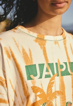 Close-up of a person wearing an orange and white tie-dye shirt with green text and an orange palm tree graphic.