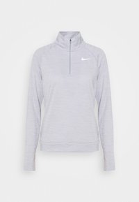 Vaaleanharmaa Nike-huppari, jossa on korkea kaulus ja puolivetoketju. Hupparissa on pitkät hihat ja pieni valkoinen logo vasemmassa rinnassa.