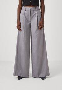 Pantalons larges gris clair avec des rayures verticales, devant plissé et coupe cintrée. Texture lisse et finition avec passants de ceinture.