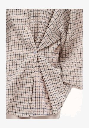 Beige plaid shirt with blue and red lines, crumpled and buttoned at the center, worn over light-colored pants.
