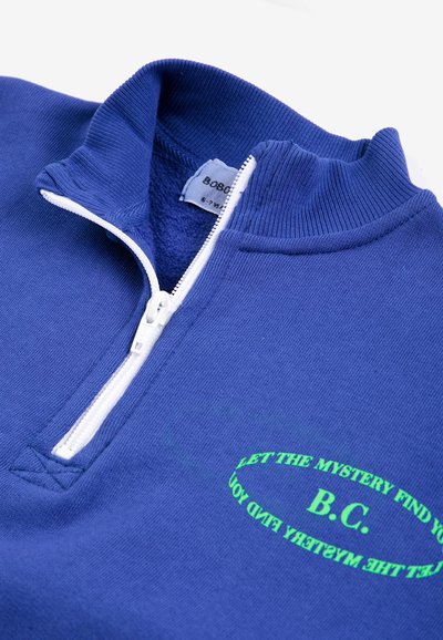Sweat-shirt bleu à fermeture éclair quart, fermeture éclair blanche et texte vert affichant "LET THE MYSTERY FIND YOU B.C." sur la poitrine.