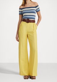 Blusa de rayas azul y blanca con hombros al aire, que se combina con pantalones anchos amarillos. Cinturón marrón con hebilla redonda que acentúa la cintura.